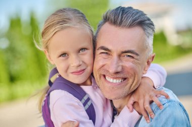 Mutlu adam çömelmiş tatlı kızına sarılıyor.