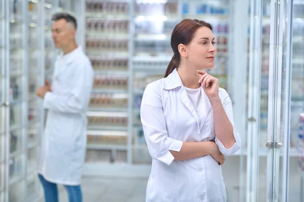 Mujer pensativa en uniforme y empleado en la farmacia —  Fotos de Stock