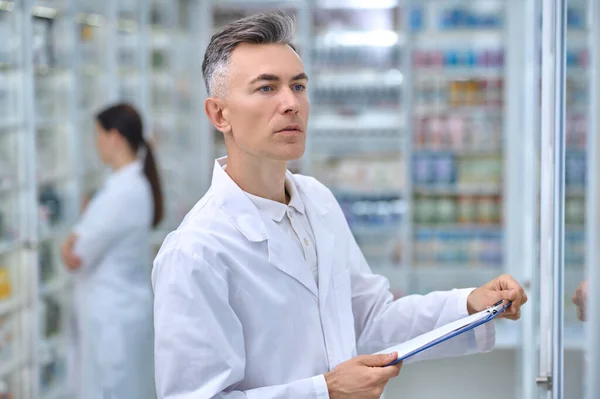 Человек с папкой смотрит на полки с лекарствами — стоковое фото