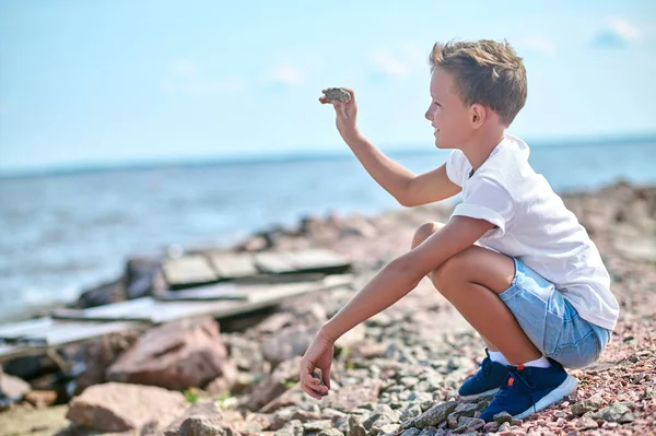 Un chico con una camiseta blanca tirando piedras al río — Foto de Stock