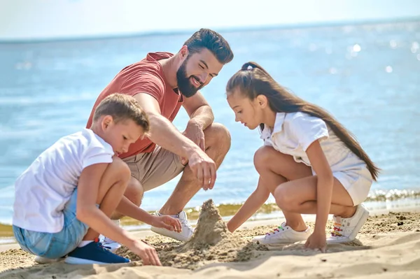 Een vader met kinderen die zandkastelen maken — Stockfoto