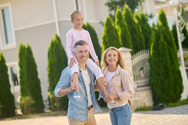 Kızı omuzlarında taşıyan bir adam ve karısı