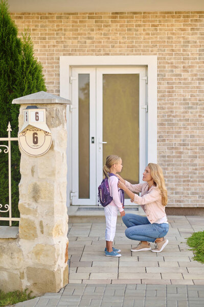 Woman crouching near daughter adjusting her backpack