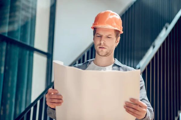 Homem em capacete de proteção olhando de perto para o plano de construção — Fotografia de Stock