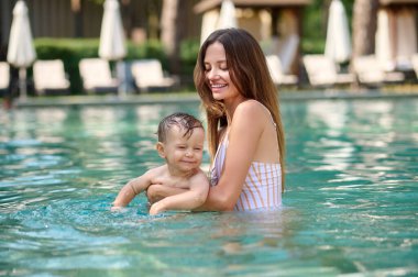 Küçük oğluyla havuzda yüzen uzun saçlı genç bir kadın.
