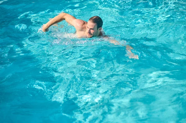 Ein junger Mann mit Sonnenbrille schwimmt in einem Pool — Stockfoto
