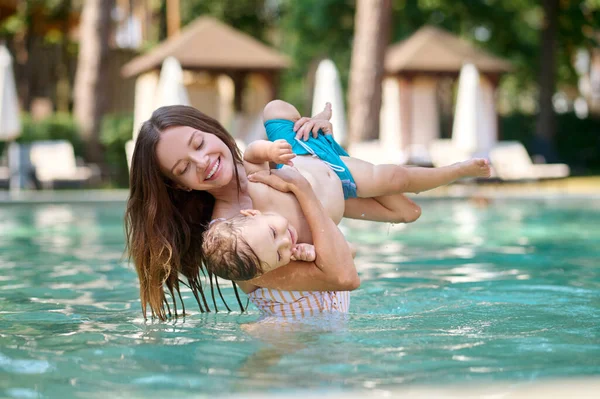 Genç bir kadın çocuğunu kucağında tutuyor ve havuzda yüzerken kendini iyi hissediyor.