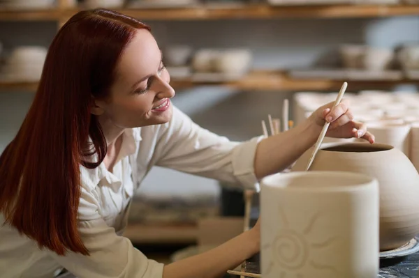 A cute female potter looking involved while painting the pot — Stock Photo, Image