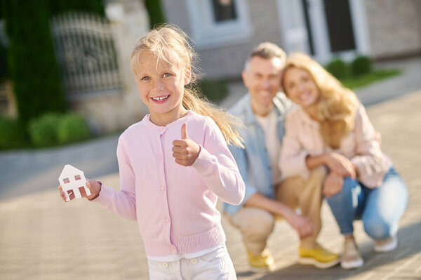 Girl showing house sign and parents behind