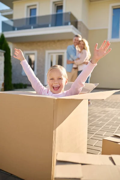Emotional girl with raised hands sitting in box — Stock Photo, Image