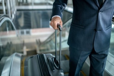 Bavulu yürüyen merdivende tutan adam yukarı çıkıyor.