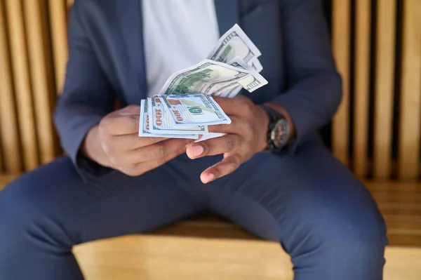 A man sitting on the bench and holding dollars in hands — Stock Photo, Image