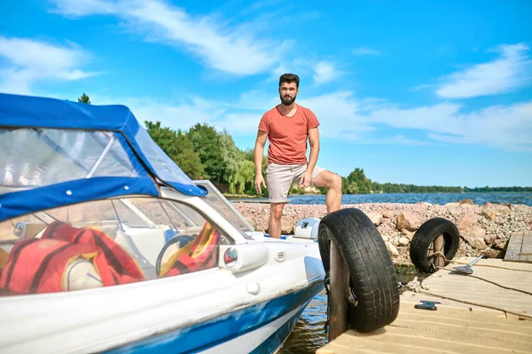 A dark-haired man standing on a dock near the boat — Stock Photo, Image