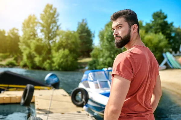 A dark-haired man standing on a dock near the boat — Stock Photo, Image