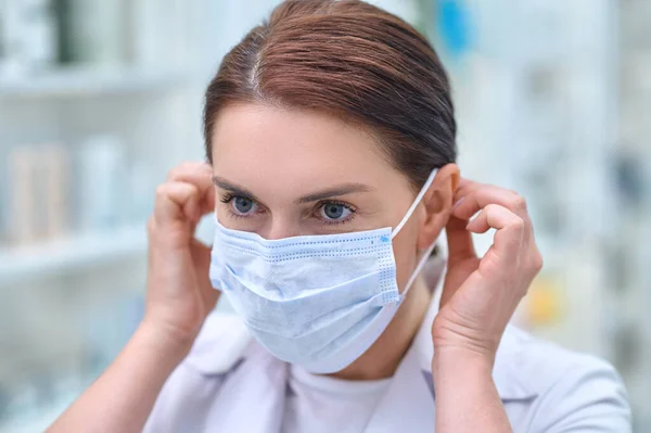 Frau, die in Apotheke arbeitet, setzt Schutzmaske auf — Stockfoto