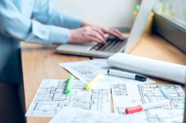 Pencere kenarında inşaat planı ve dizüstü bilgisayarın yanında kadın eli.