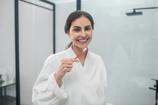 En ung vacker kvinna i vit badrock borstar tänderna — Stockfoto