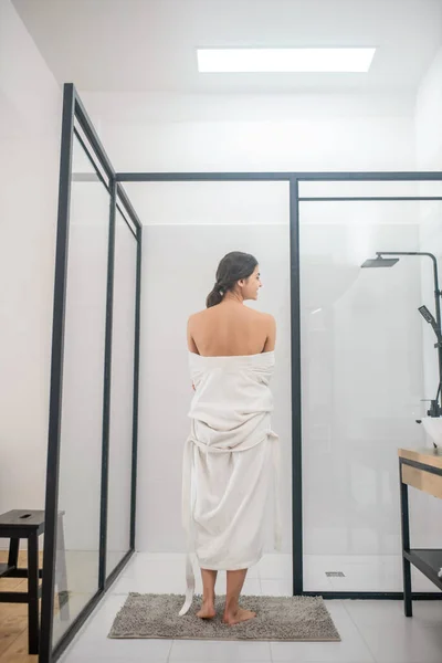 Ein dunkelhaariges junges Mädchen im weißen Bademantel im Badezimmer — Stockfoto