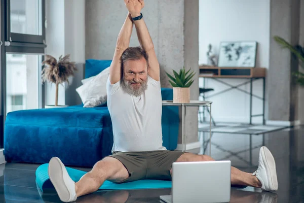 A mature man having online workout and stretching — Stock Photo, Image