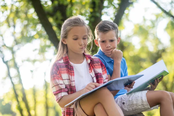 Серьезный мальчик и девочка с учебниками на открытом воздухе — стоковое фото