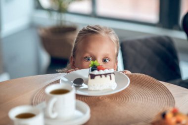 Tatlı sarışın bir kız pasta dilimine bakarken heyecanla bekliyor.