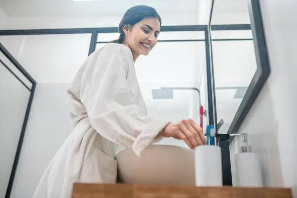 Een vrouw in een wit badjas doet ochtend procedures in de badkamer — Stockfoto