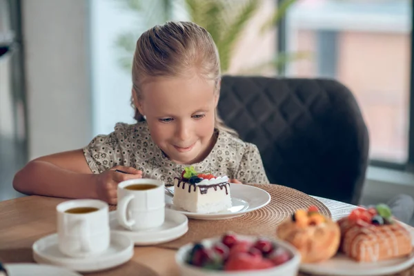 A cute blonde girl looking anticipated while looking at the slice of cake — Stock Photo, Image