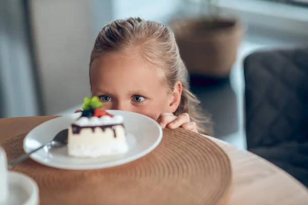 A cute blonde girl looking anticipated while looking at the slice of cake — Stock Photo, Image