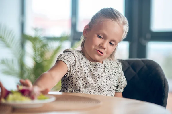 Ein kleines Mädchen schaut unzufrieden auf das Essen auf dem Tisch — Stockfoto