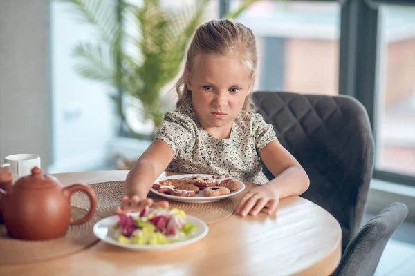 A small girl looking unpleased while looking at the food on the table — Stock Photo, Image