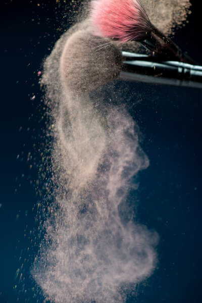 Professional black make-up brush with pink powder in motion isol