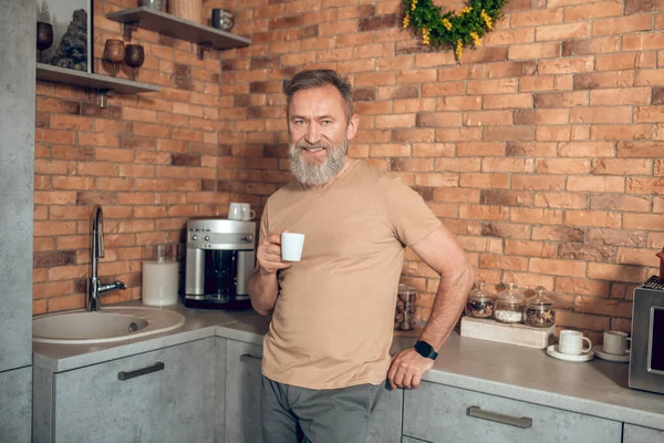 En midagedman som står i köket med en kaffekopp i händerna — Stockfoto