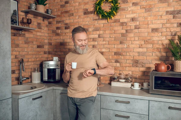 Een tussenpersoon die in de keuken staat met een koffiebeker in handen — Stockfoto