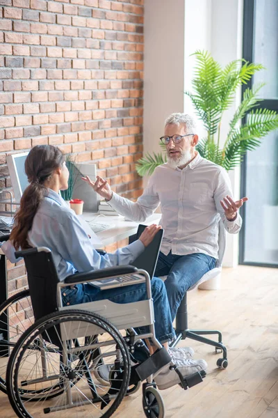 Een meisje in een rolstoel praten met haar mannelijke collega en kijken betrokken — Stockfoto