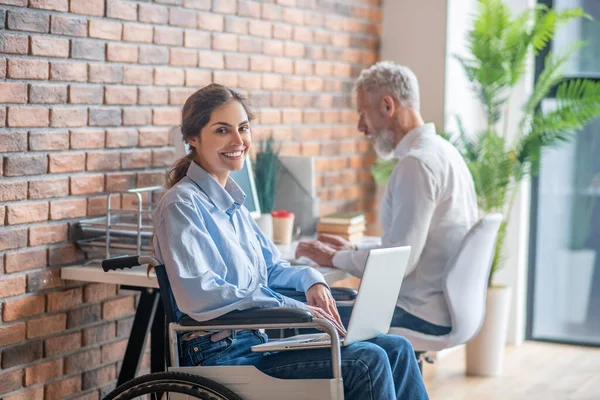 A girl on a wheelchair talking to her male colleague and looking involved — Stock Photo, Image