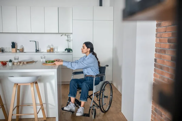 Una linda chica en una silla de ruedas en la cocina en casa — Foto de Stock