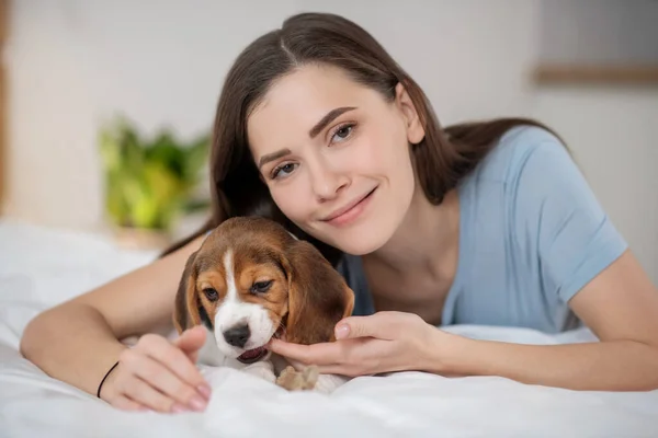 En husdjursägare sitter på sängen och fäller nöjd med sitt husdjur — Stockfoto