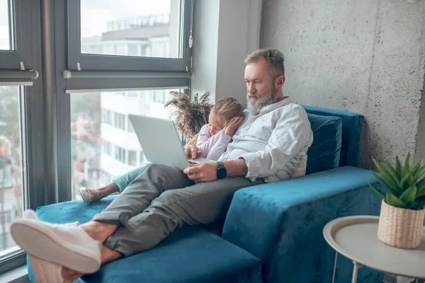 Ein Mann arbeitet, während seine kleine Tochter neben ihm sitzt — Stockfoto