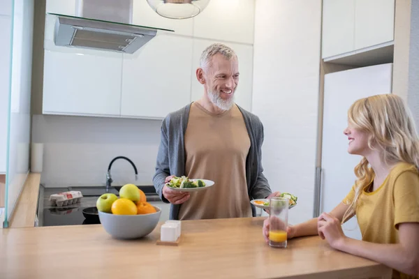 A bearded man holding two plates and offering food to his daughter — Stock Photo, Image