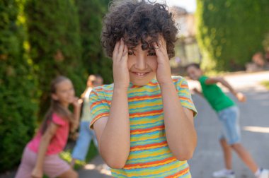 Gülümseyen çocuk avuçlarla yüzünü kapatıyor ve arkadaşlarını saklıyor.