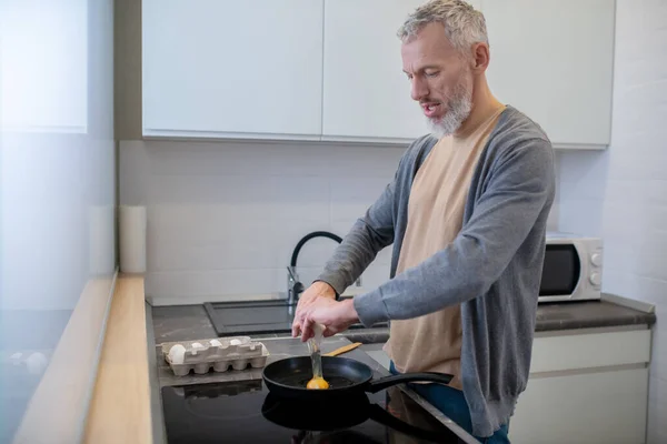 Um homem de cabelos grisalhos a cozinhar omlette na cozinha — Fotografia de Stock