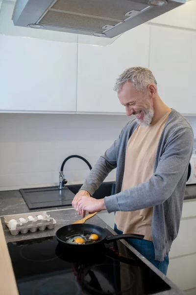 Un hombre de pelo gris cocinando omlette en la cocina — Foto de Stock