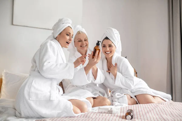 Mujeres alegres en la cama mirando el producto cosmético — Foto de Stock