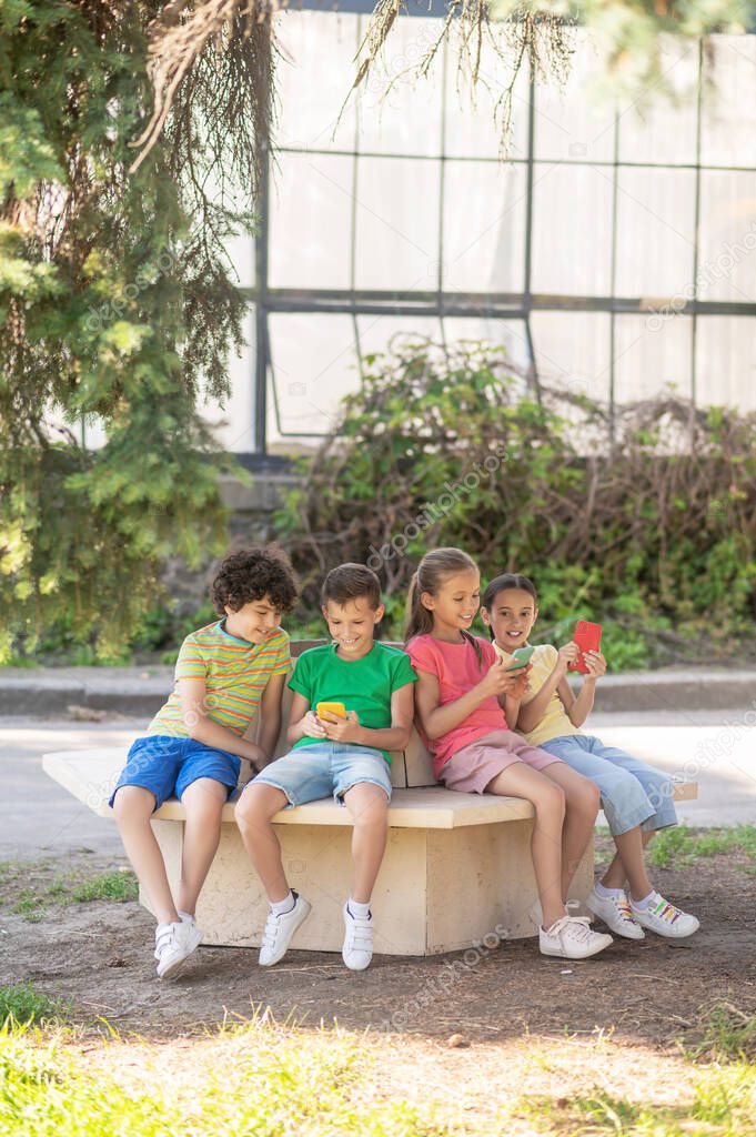 School children with smartphones sitting in park