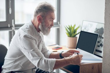 Olgun bir iş adamı evden çalışıyor ve belgeleri inceliyor.