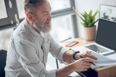 Olgun bir iş adamı evden çalışıyor ve belgeleri inceliyor.
