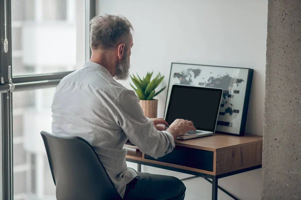 Een volwassen man in wit tshirt werkend op een laptop — Stockfoto