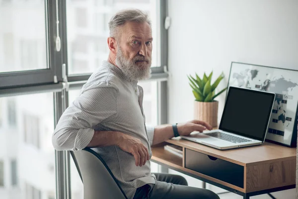 Ein reifer Mann im weißen T-Shirt arbeitet an einem Laptop — Stockfoto