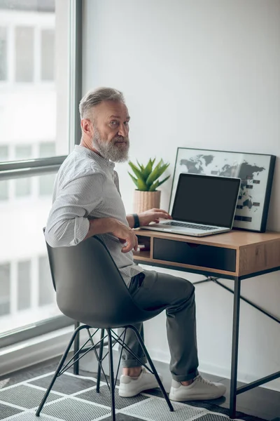 Un uomo maturo in camicia bianca che lavora su un computer portatile — Foto Stock