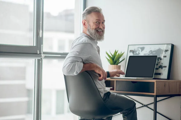 Un uomo maturo in camicia bianca che lavora su un computer portatile — Foto Stock